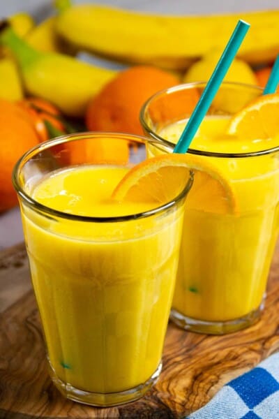 Banana mango smoothie in two glasses with fresh orange on the side.
