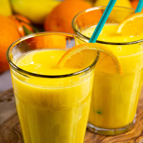 Banana mango smoothie in two glasses with fresh orange on the side.