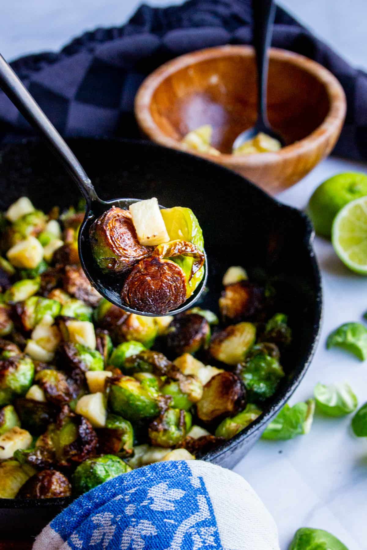 Crispy roasted brussel sprouts on a spoon over a cast iron pan.