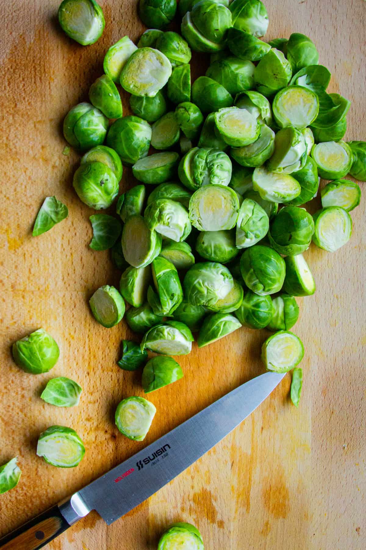 Cutting the brussel sprouts on a wooden board with a knife.