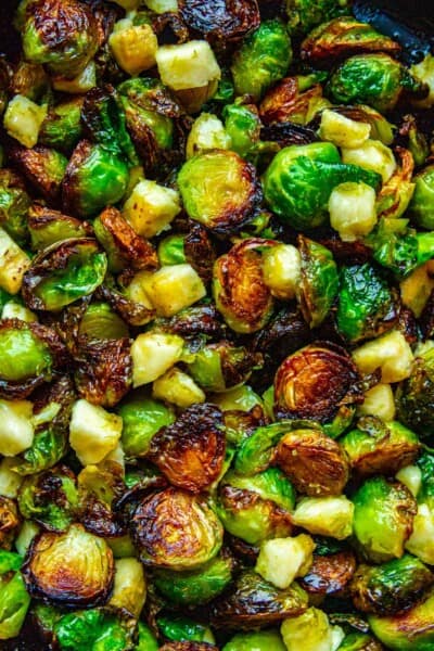 A close up shot of crispy roasted Brussel sprouts with banana and lime in a cast iron pan.