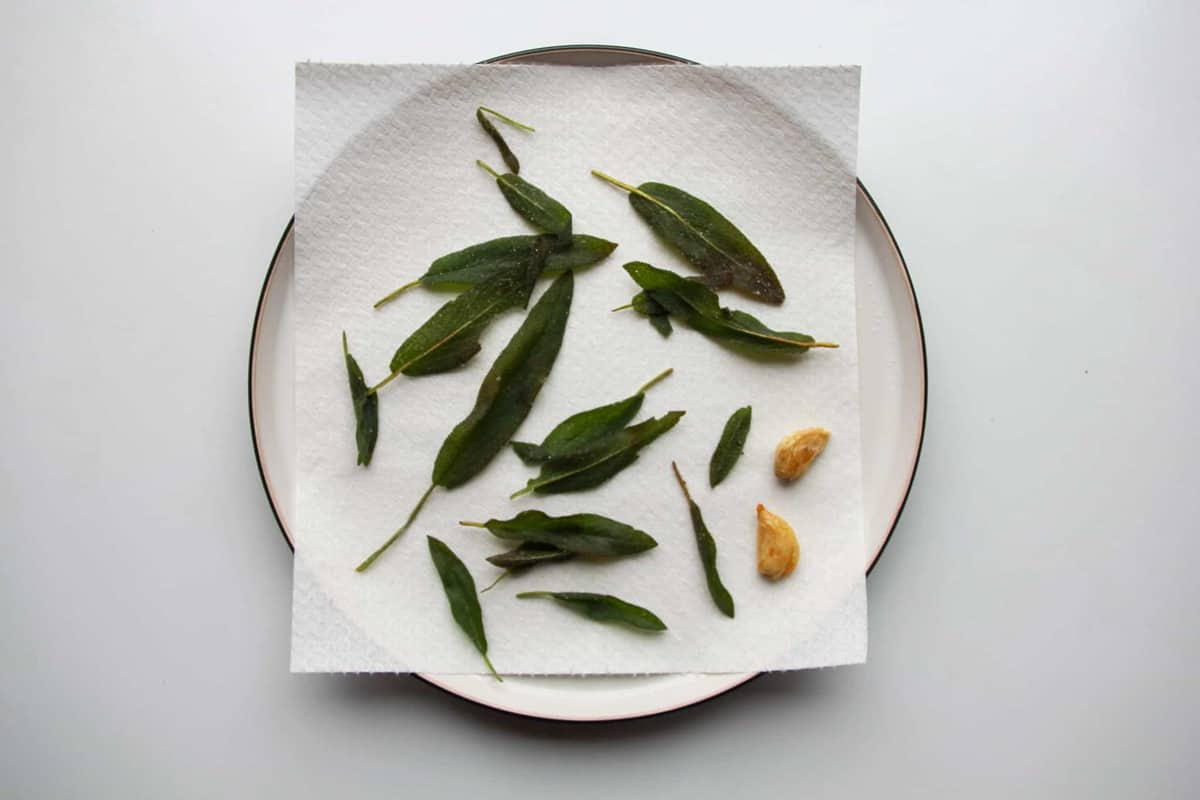 The fried sage leaves and garlic on paper towel a plate.