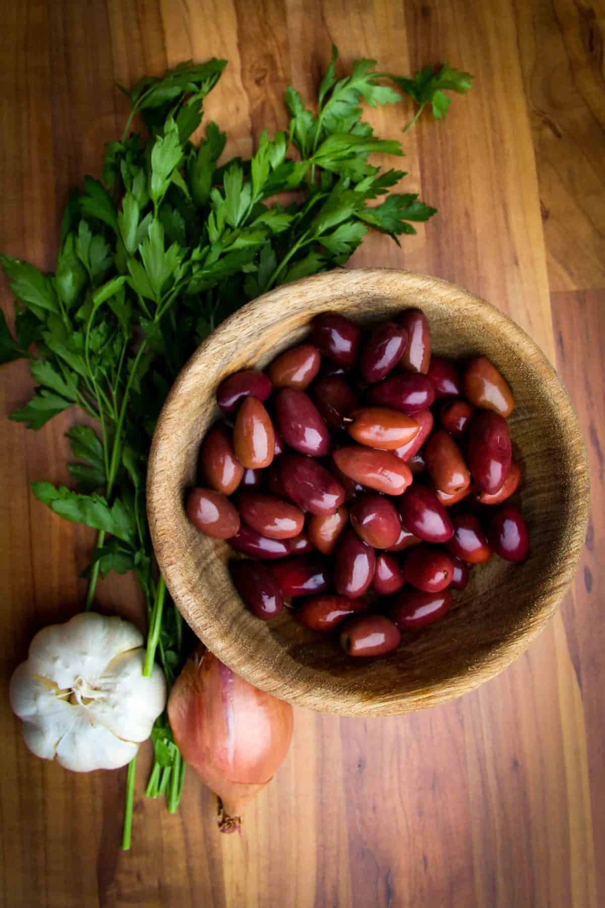 Olives, parsley, garlic and shallots all raw on a table.