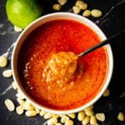Peanut sauce in a bowl with peanuts around.