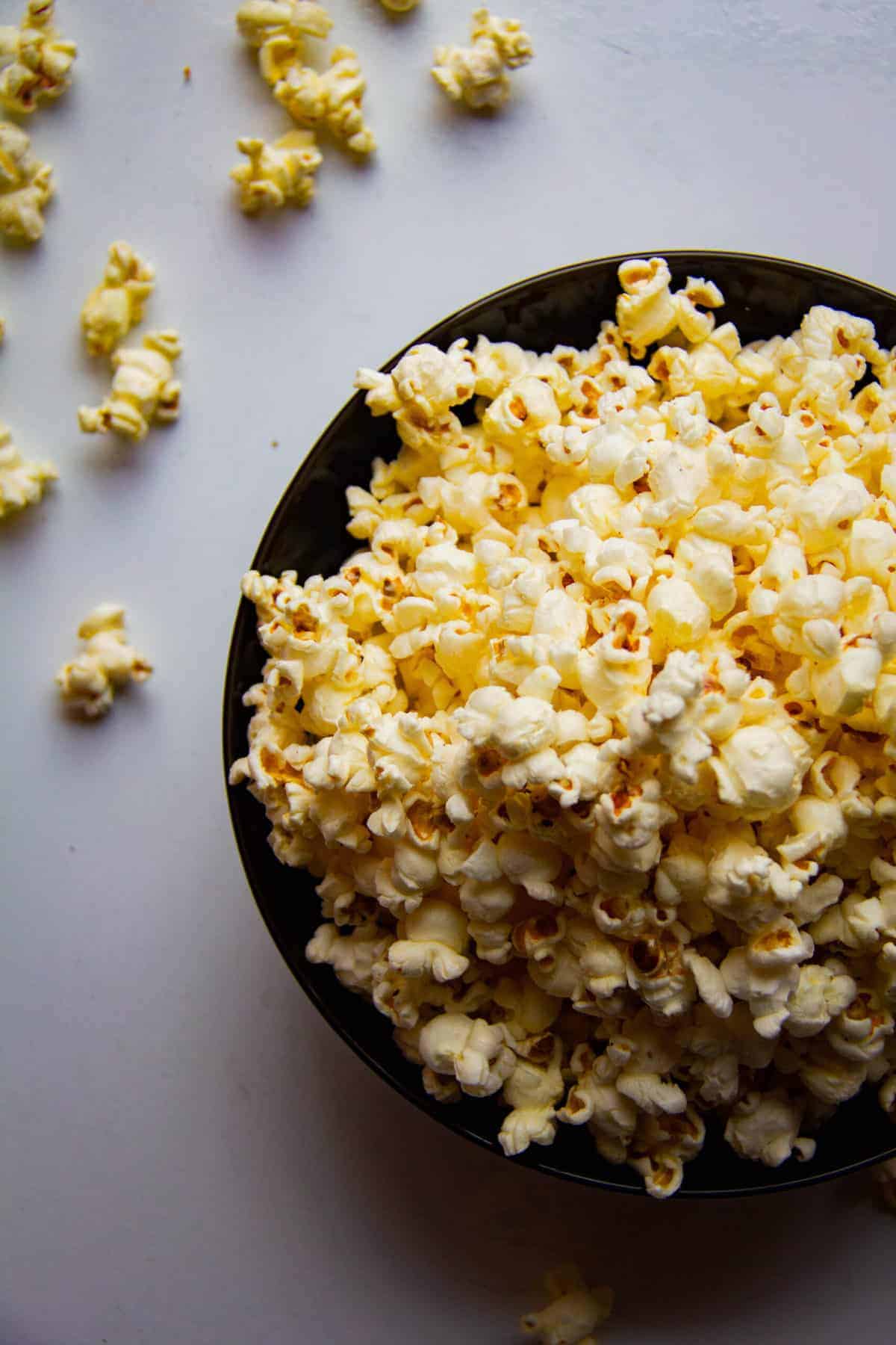 Popcorn in a bowl with some spilling out the sides.