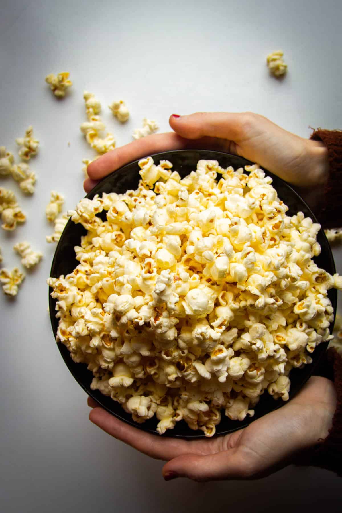 Buttery stovetop popcorn in a bowl being held by two hands.