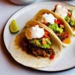 Instant pot carnitas in soft tacos with guacamole, tomato salsa and creme fraiche on top.