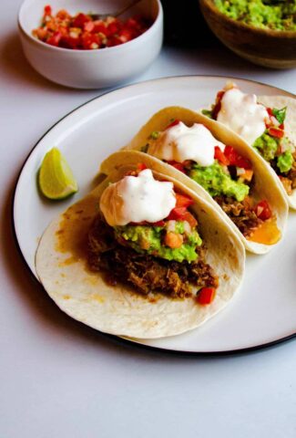 Instant pot carnitas in soft tacos with guacamole, tomato salsa and creme fraiche on top.