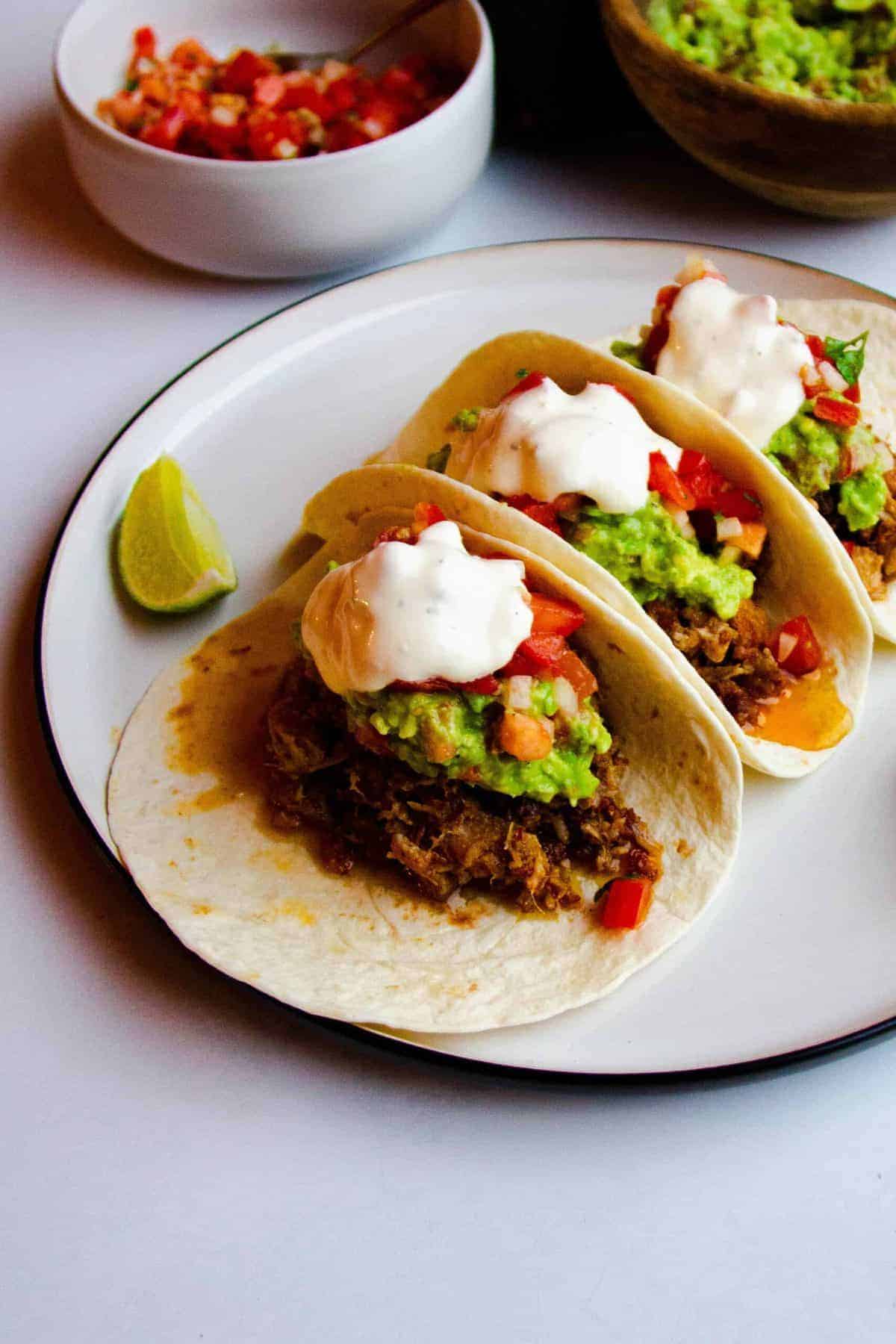 Instant pot carnitas in soft tacos with guacamole, tomato salsa and creme fraiche on top.