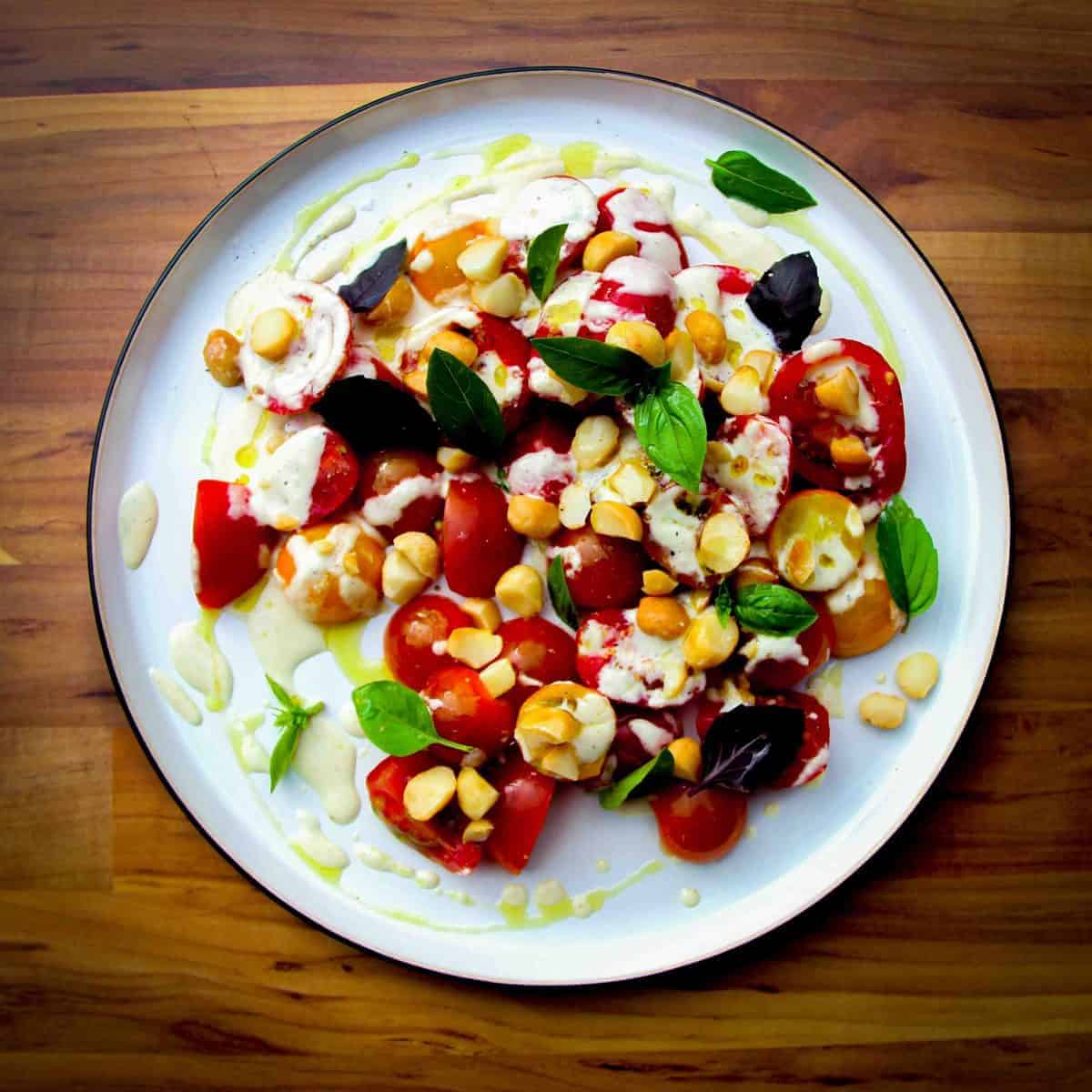 A tomato salad on a plate with basil and a macadamia dressing.