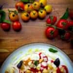 A tomato salad with macadamia dressing on a plate with fresh tomatoes on the side.