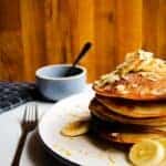 Vegan banana pancakes stacked high on a plate with almonds, fresh banana and maple syrup.