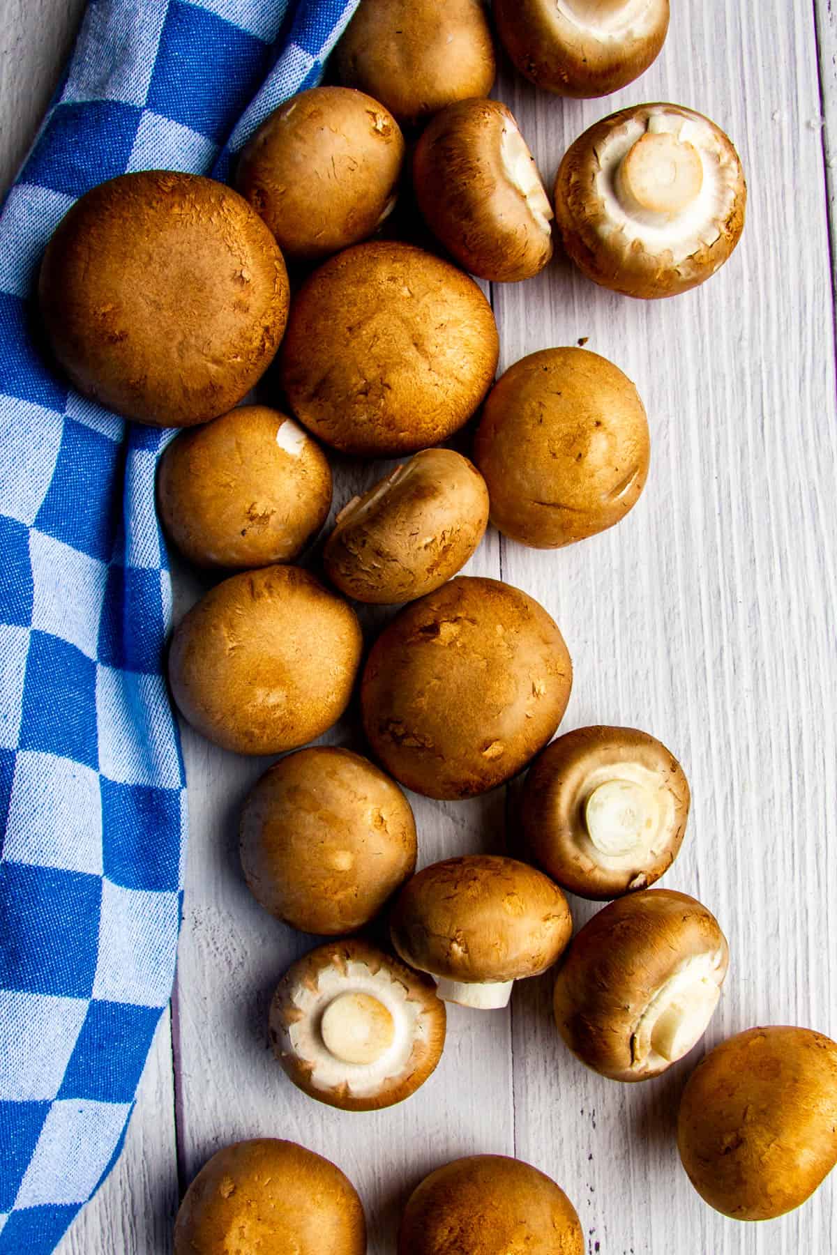 Raw mushrooms on a white wooden board with a blue towel beside.