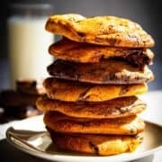 A stack of my ultimate chocolate chip cookies with a glass of milk behind it.