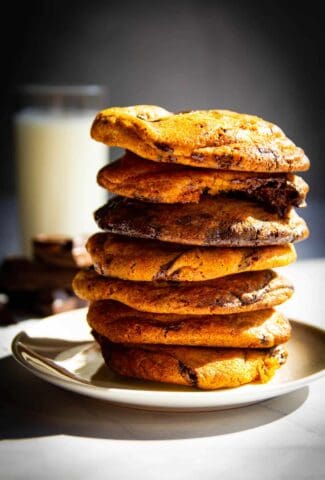 A stack of my ultimate chocolate chip cookies with a glass of milk behind it.