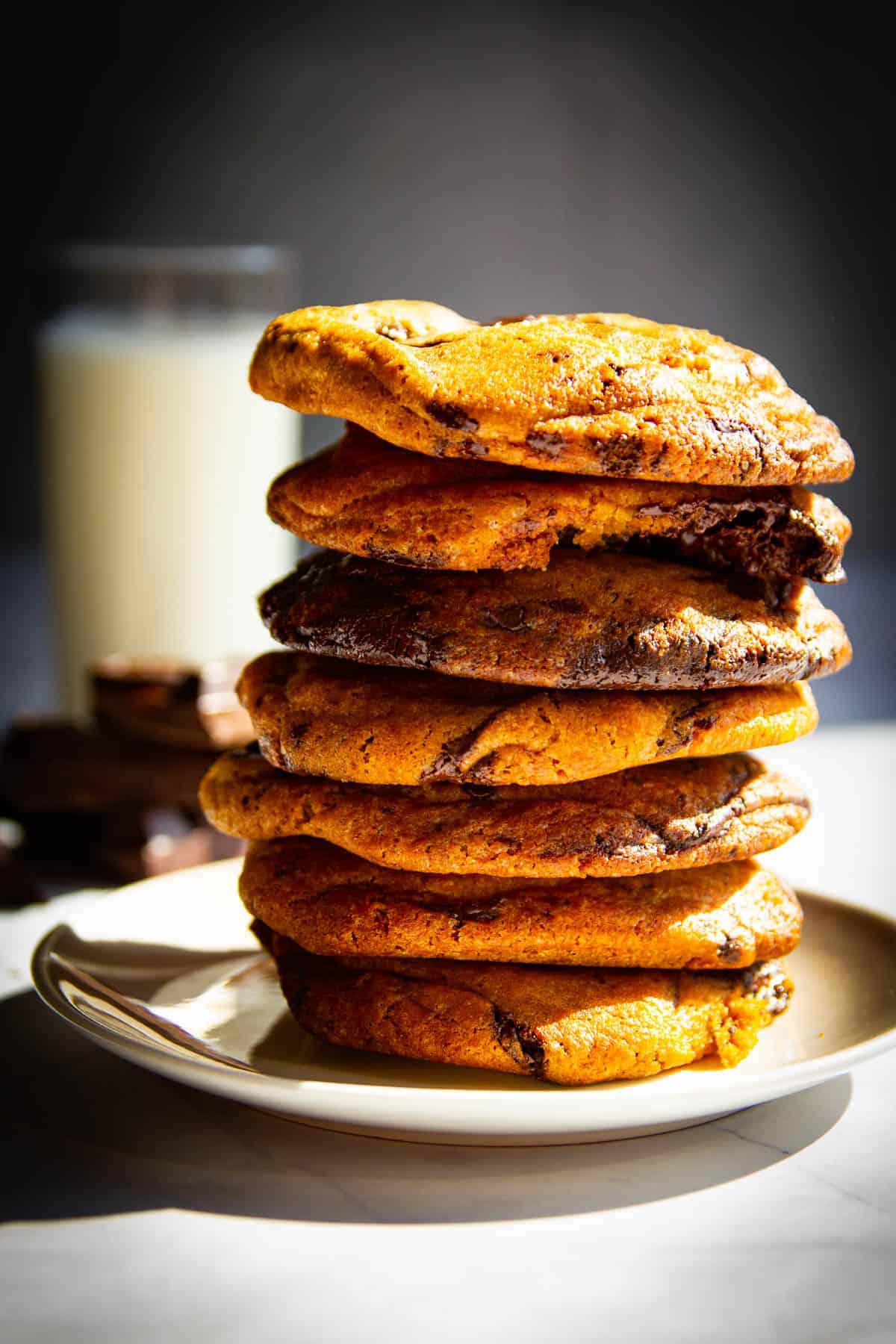 A stack of my ultimate chocolate chip cookies with a glass of milk behind it.