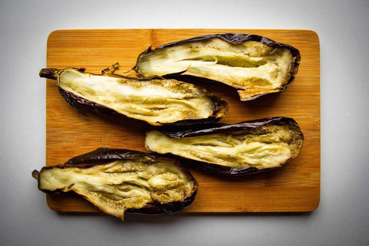The roasted eggplants split in half on a board.