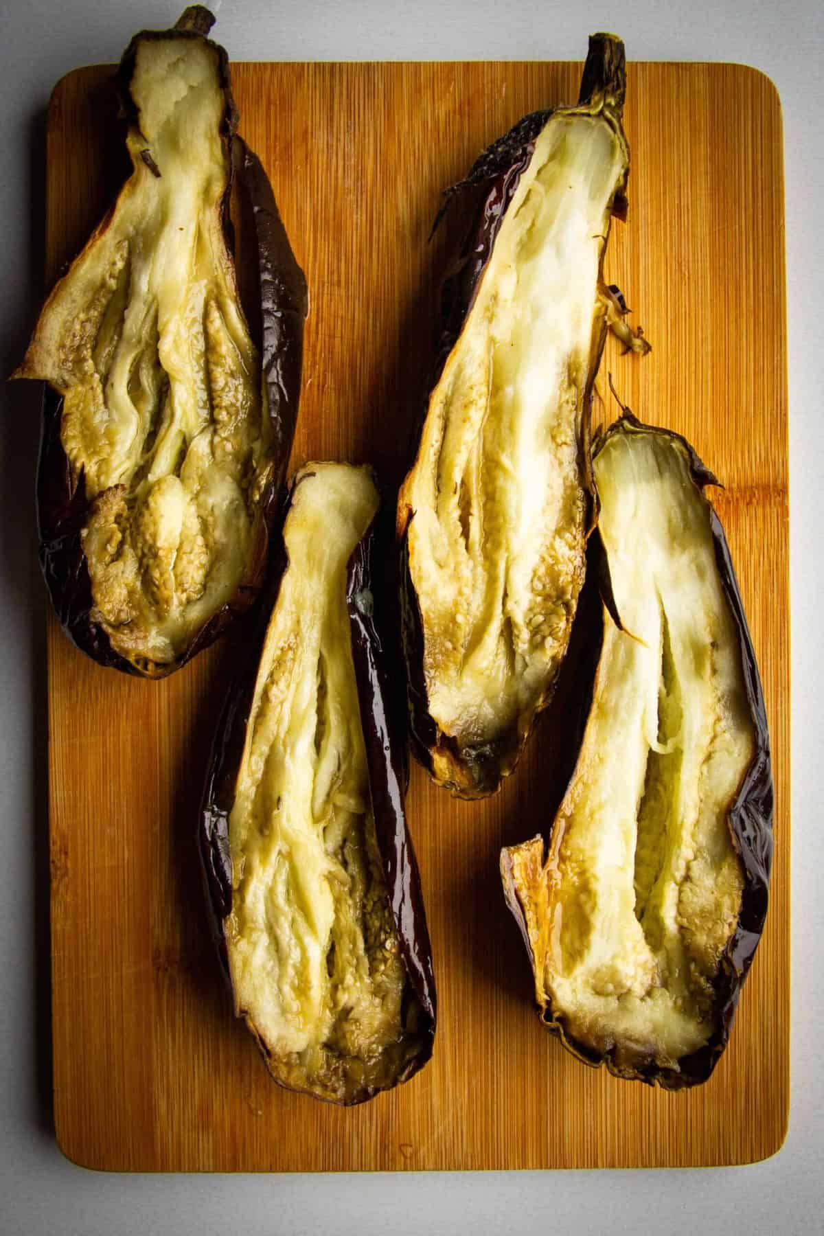 The roasted eggplants split in half on a board.