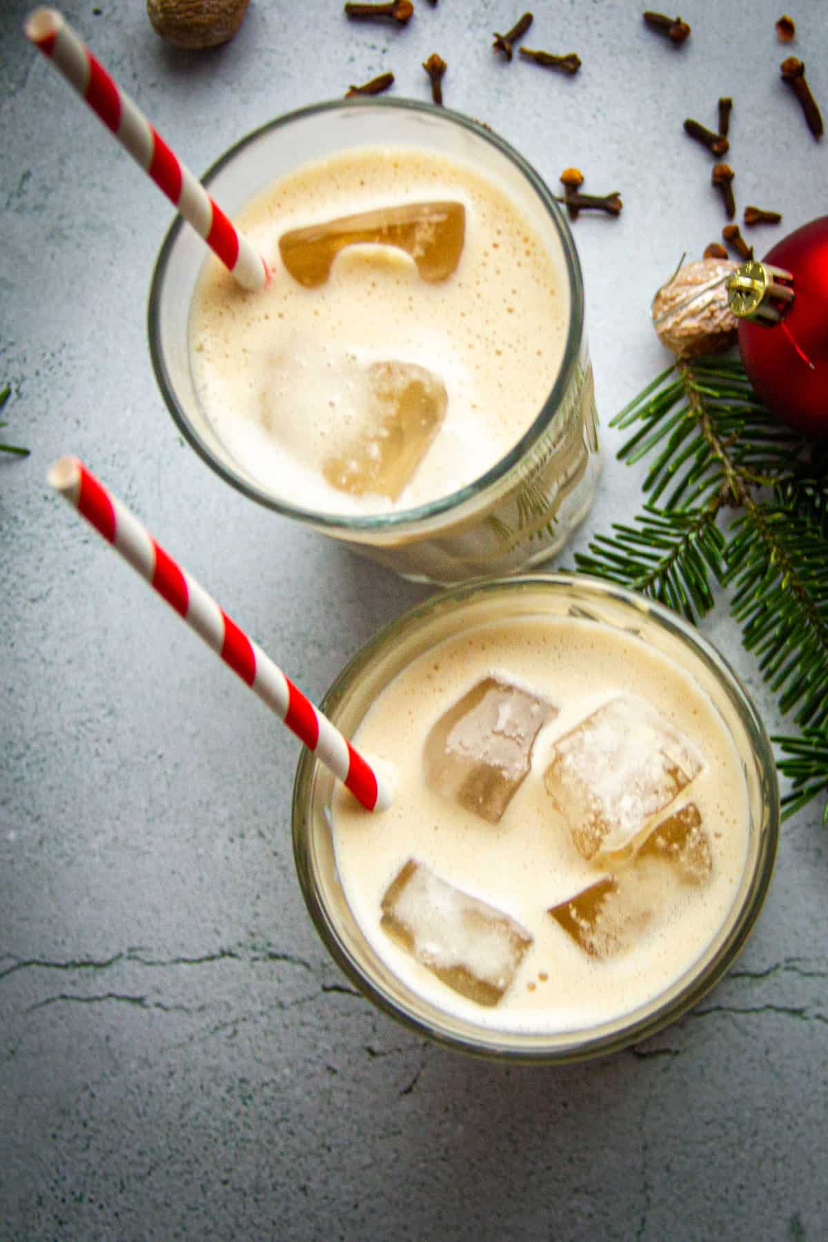 Top down shot of two glasses of oat milk eggnog with striped paper straws.