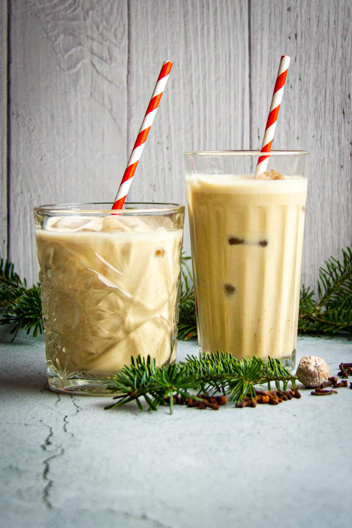 Oat milk eggnog in two glasses with striped paper straws.