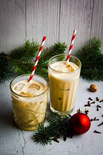 Two glasses of oat milk eggnog with Christmas decorations.