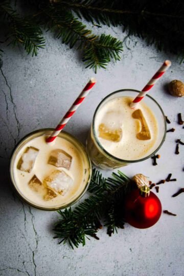 Two glasses of oat milk eggnog with Christmas decorations.