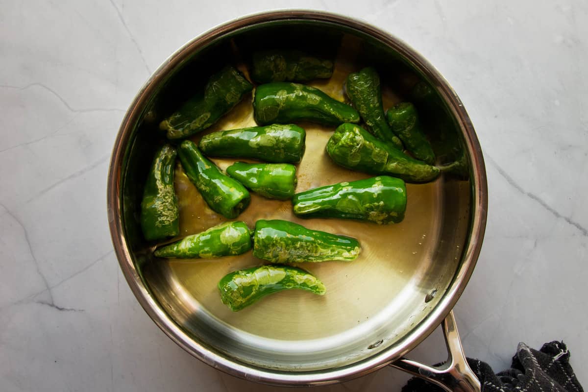 Blistering the peppers in the pan with olive oil.