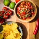 Pico de gallo, tortilla chips, chili, tomato and fresh limes on the table.