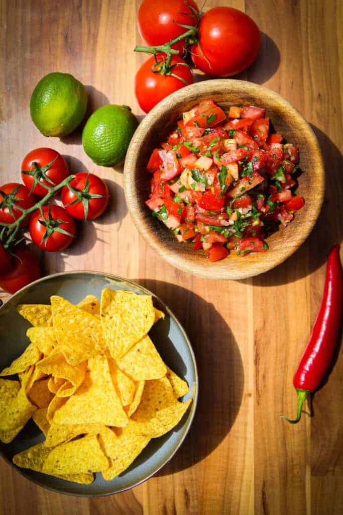 Pico de gallo, tortilla chips, chili, tomato and fresh limes on the table.