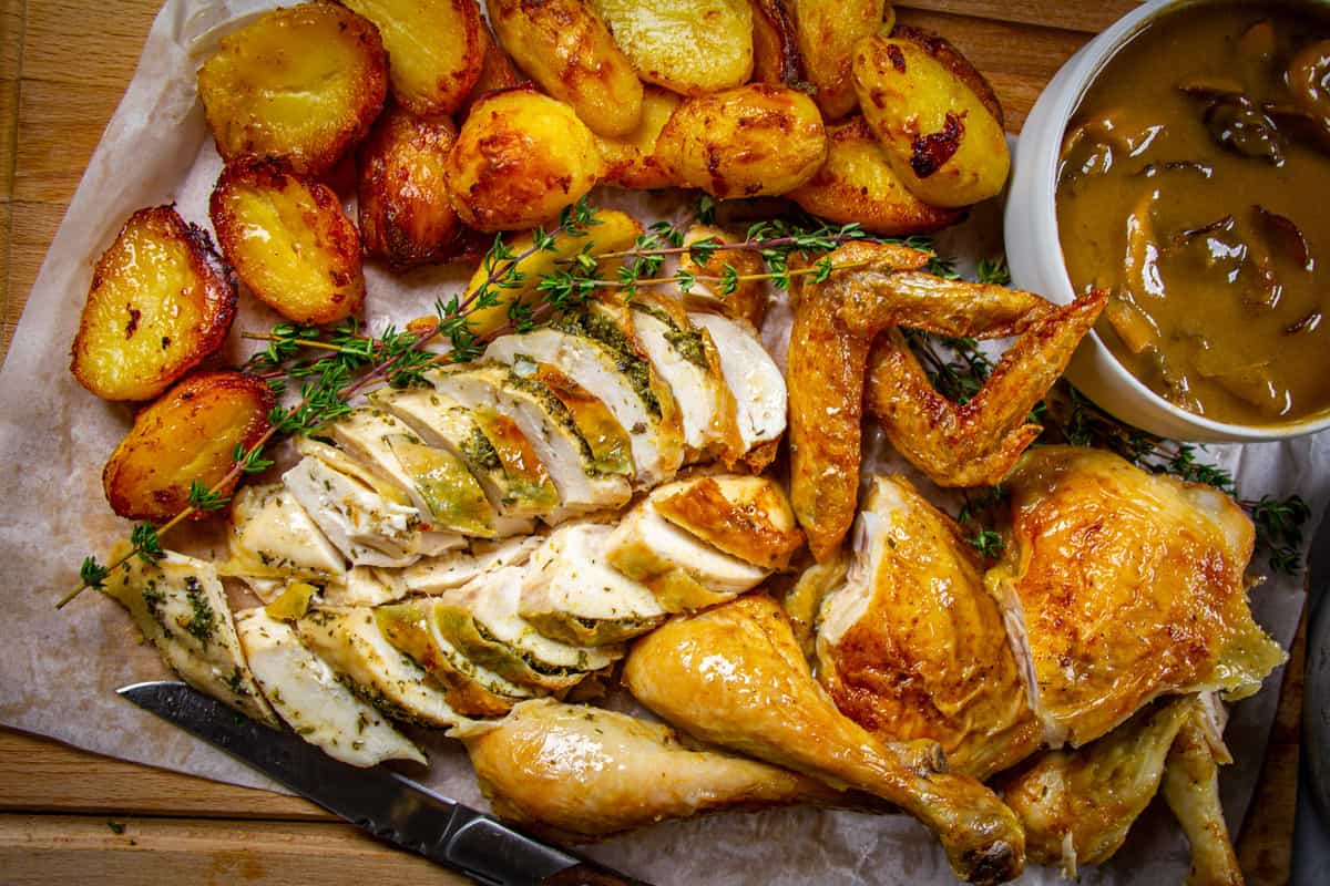 Spatchcock holiday chicken dinner sliced on a board with crispy potatoes and fresh thyme around.