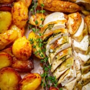 Spatchcock holiday chicken dinner sliced on a board with crispy potatoes and fresh thyme around.