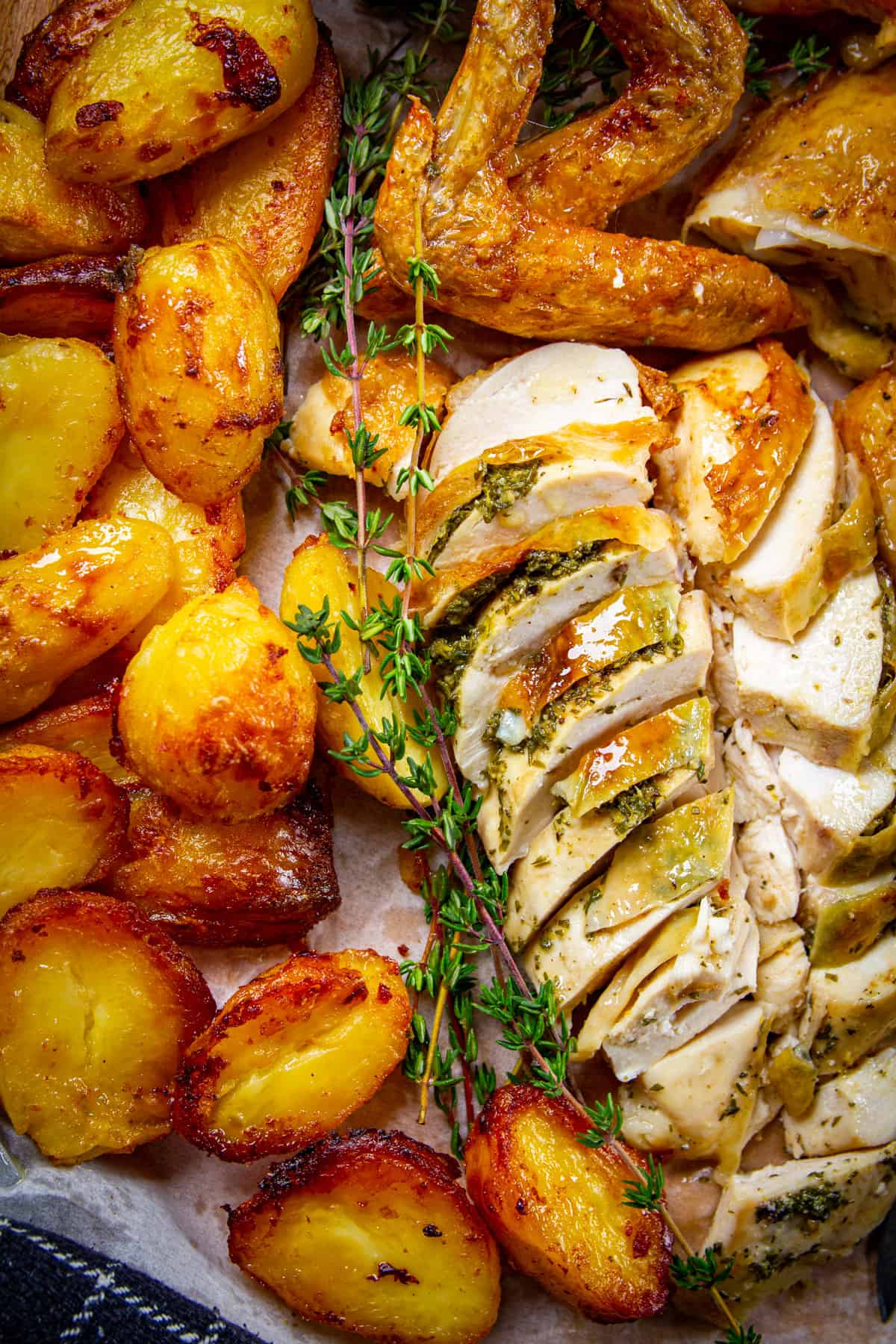Spatchcock holiday chicken dinner sliced on a board with crispy potatoes and fresh thyme around. 