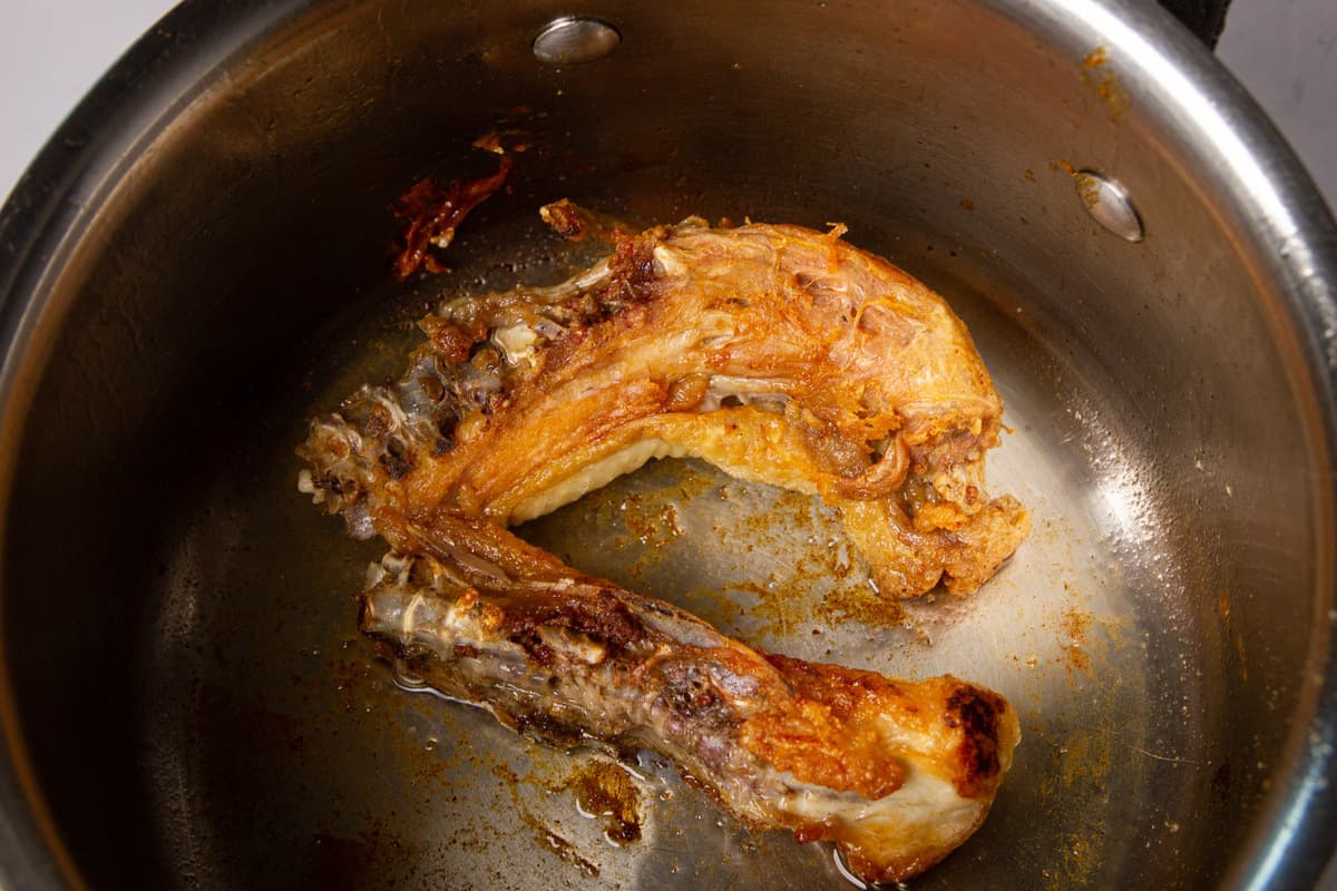 The browned chicken back in a pan.