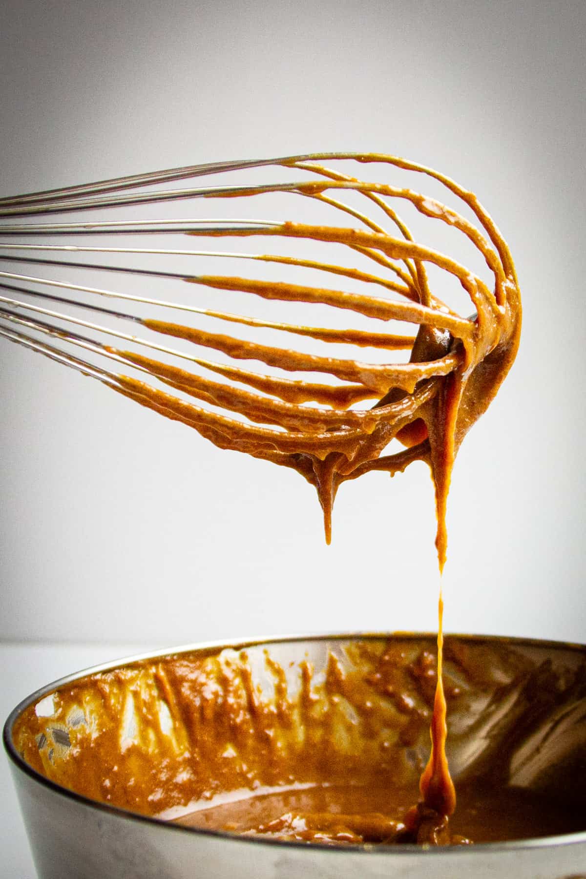 A whisk with the sticky toffee pudding batter on it.