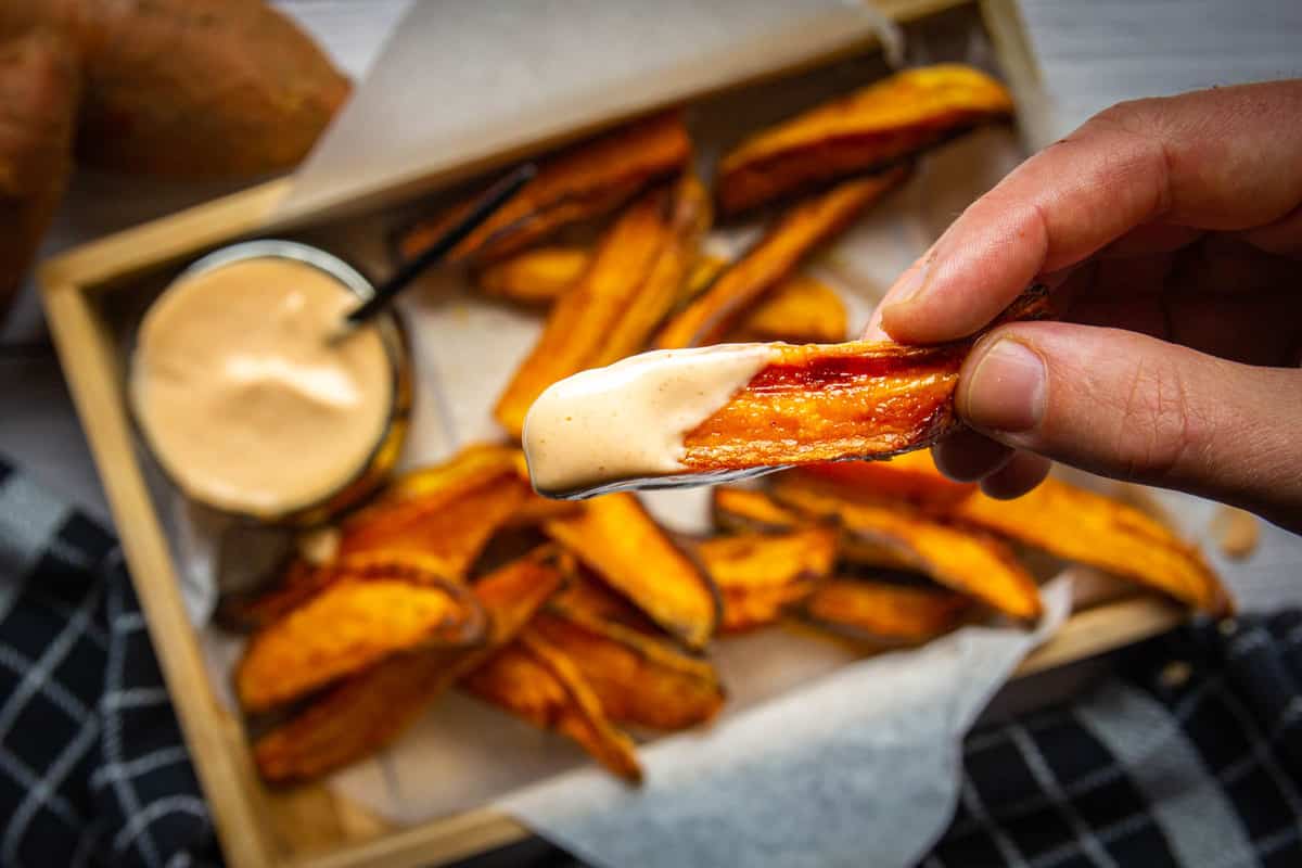 Crispy baked sweet potato wedges with one wedge dipped in spicy mayo.