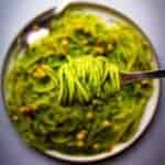 Vegan Pasta Pesto Spaghetti with hazelnuts, sweet pea and miso on a fork over a plate.