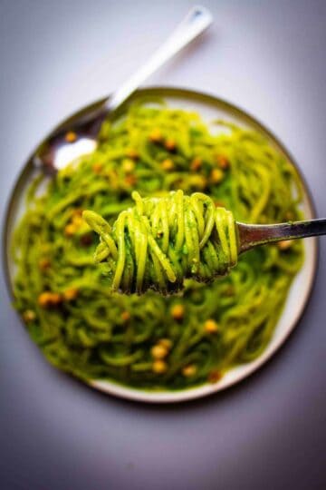 Vegan Pasta Pesto Spaghetti with hazelnuts, sweet pea and miso on a fork over a plate.