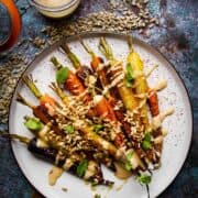 Roasted rainbow carrots on a plate with a toasted sunflower dressing on the side.