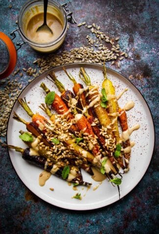 Roasted rainbow carrots on a plate with a toasted sunflower dressing on the side.