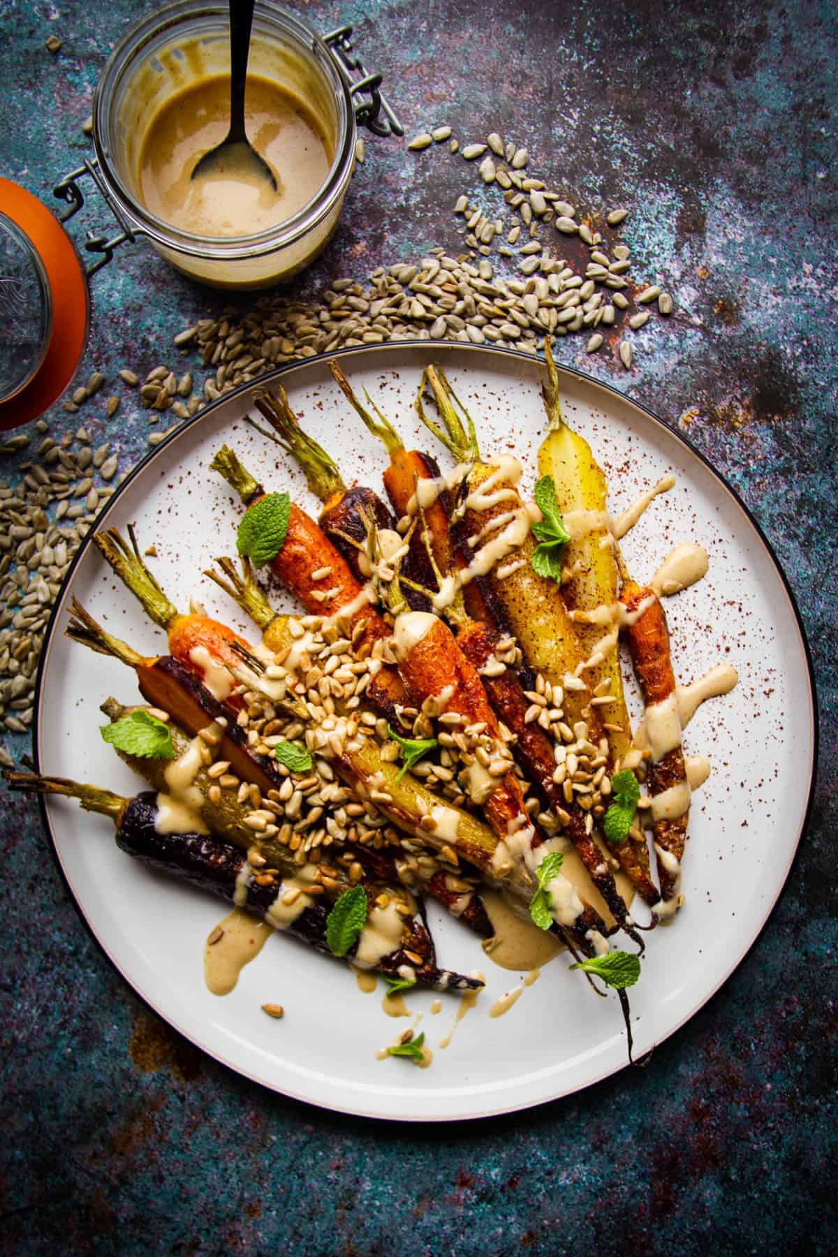 Roasted rainbow carrots on a plate with a toasted sunflower dressing on the side.