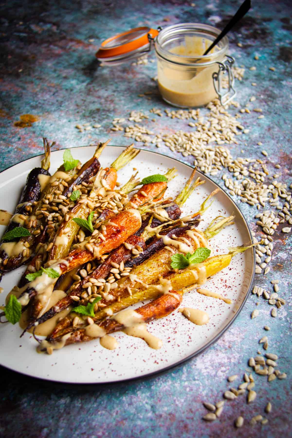 Roasted rainbow carrots on a plate with a toasted sunflower dressing on the side.