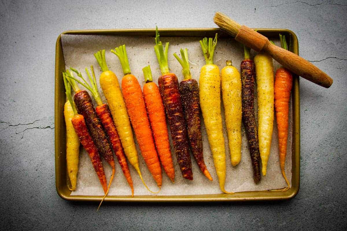 The rainbow carrots lined up on a tray with oil and salt.