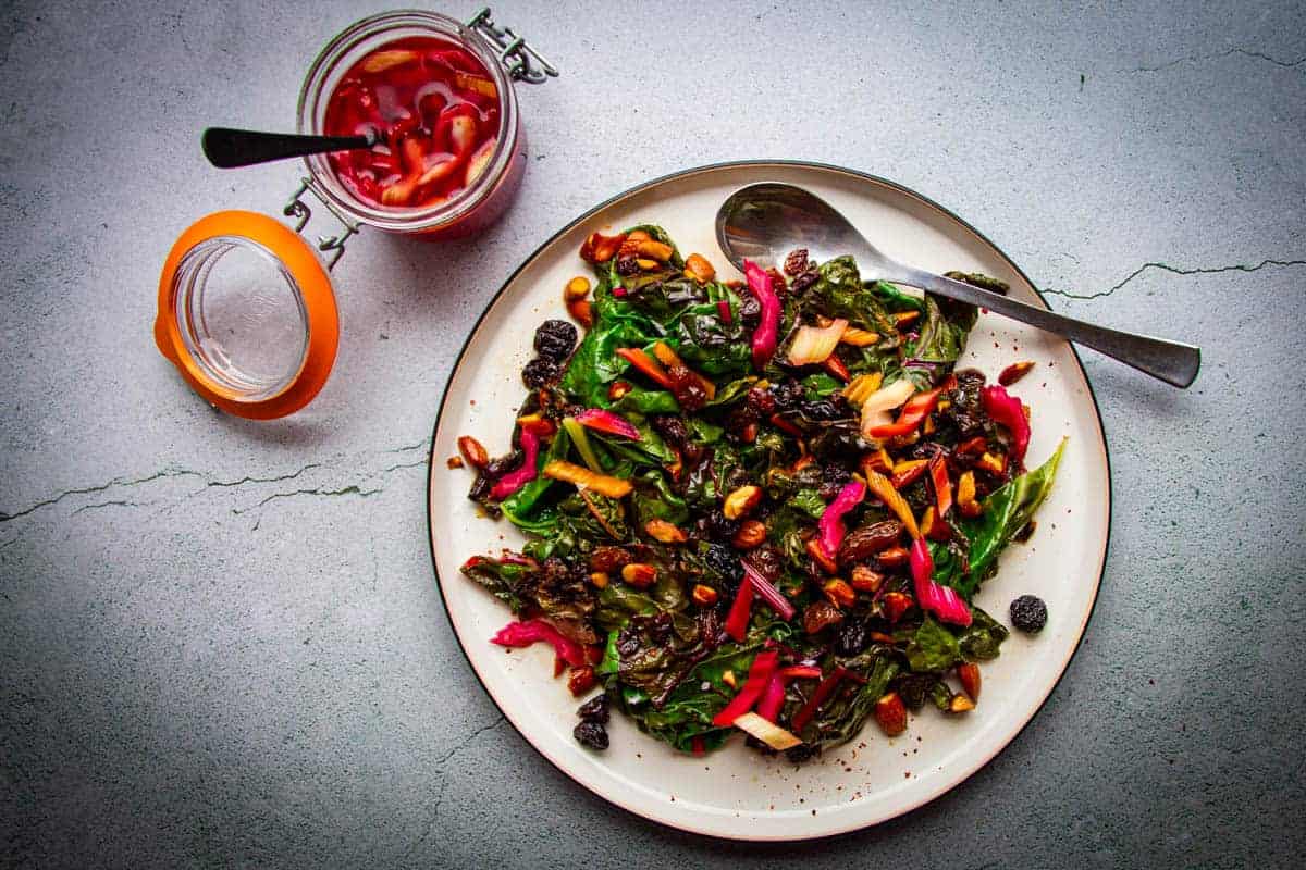 sauteed rainbow chard with brown butter raisins, almonds and chili on a plate with pickled chard stem on the side.