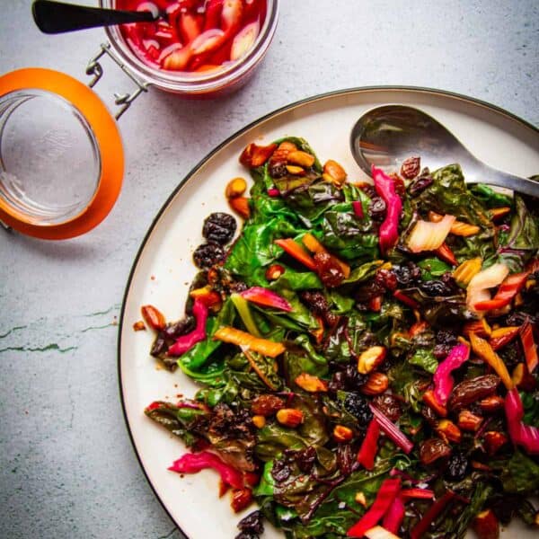 sauteed rainbow chard with brown butter raisins, almonds and chili on a plate with pickled chard stem on the side.