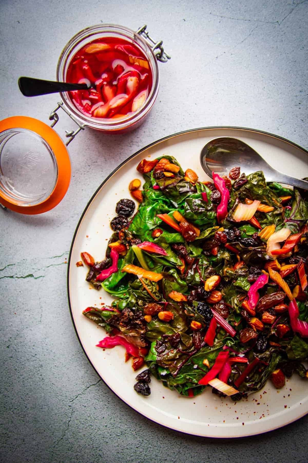 sauteed rainbow chard with brown butter raisins, almonds and chili on a plate with pickled chard stem on the side.