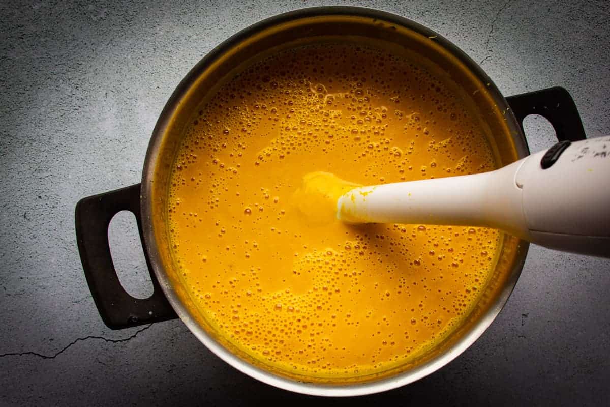 Blending the soup with a hand blender until smooth.