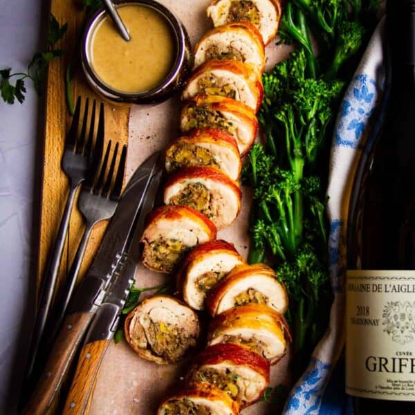 Stuffed chicken leg with bacon, herbs, porcini, walnut and a date sauce on a board with wine and broccoli.