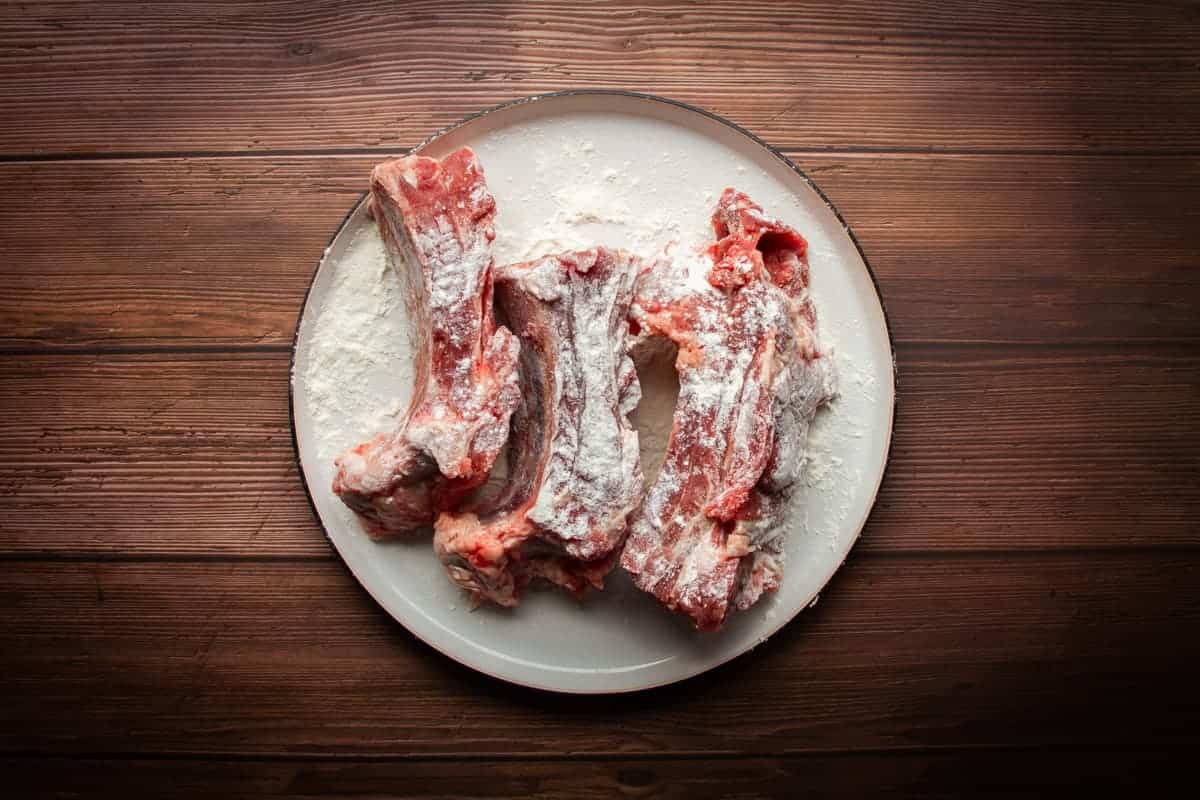 Dusting the short ribs in flour.