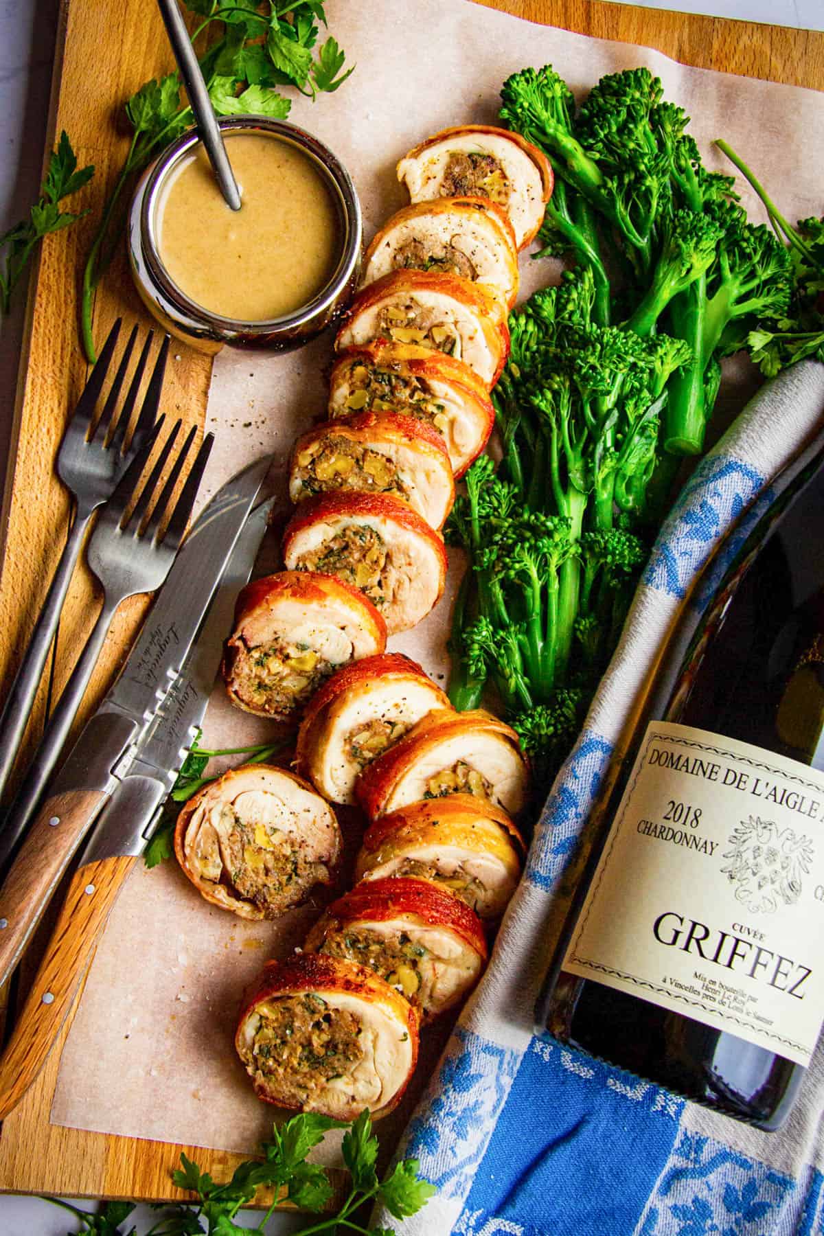 Stuffed chicken leg with dates, walnuts, bacon and a porcini sauce sliced nicely on a board with a bottle of wine beside.