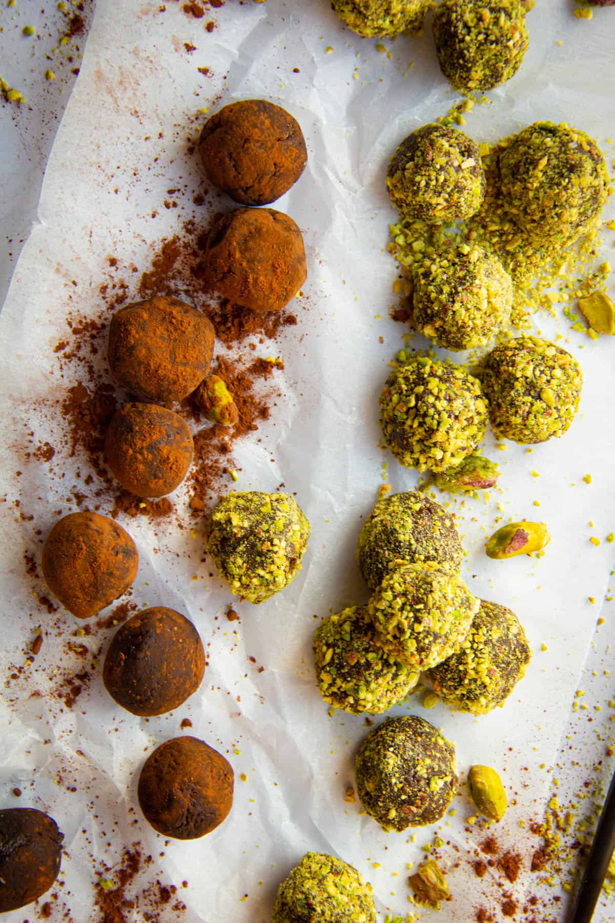 Vegan chocolate truffles with pistachio and cocoa powder on a marble slab.